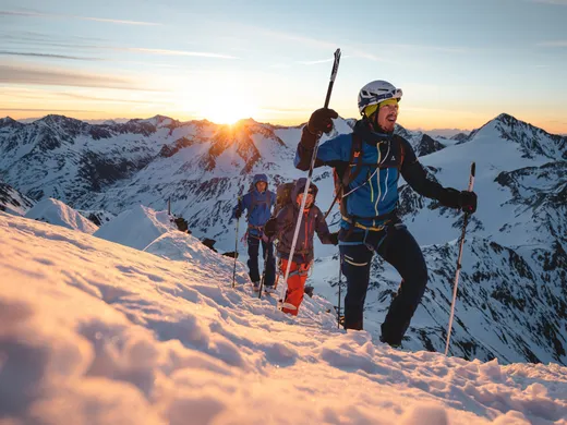 Snowy adventures on winter holidays in the Alps Gruppe von Bergsteigern mit Ausrüstung beim Aufstieg im Schnee bei Sonnenaufgang