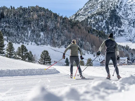 Snowy adventures on winter holidays in the Alps Zwei Personen beim Langlaufen auf verschneiter Loipe vor Bergkulisse