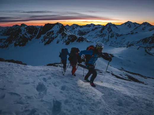 Snowy adventures on winter holidays in the Alps Drei Bergsteiger steigen bei Sonnenaufgang durch verschneite Berge