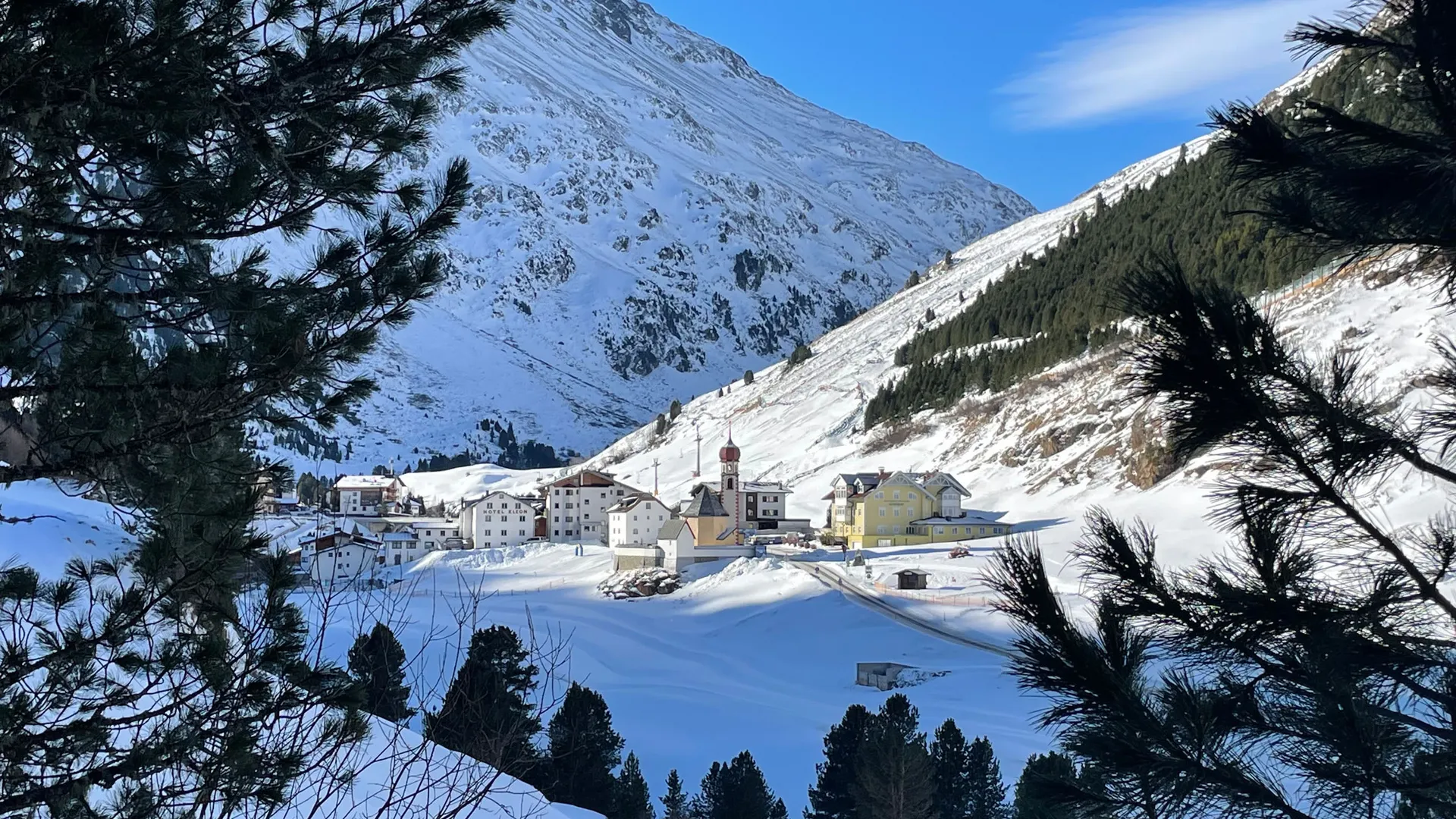 Snowy adventures on winter holidays in the Alps Snowy mountain village with church below a snow-covered peak, framed by pine trees