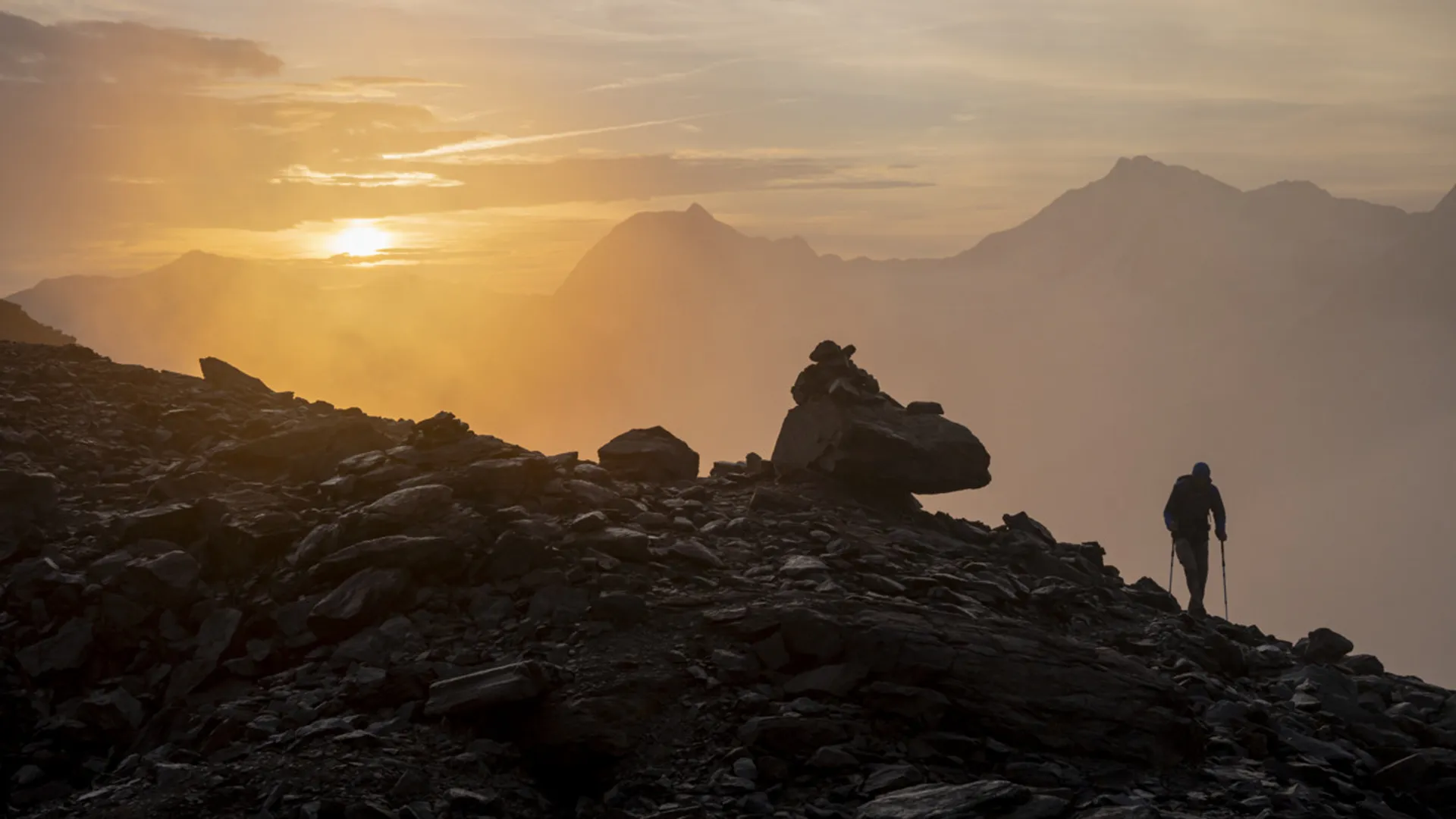 Weisskugel: dein Gasthof in Vent Wanderer auf felsigem Bergpfad bei Sonnenaufgang mit Nebel und Bergen