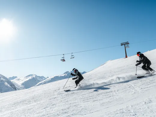 Snowy adventures on winter holidays in the Alps Zwei Skifahrer fahren bei sonnigem Wetter auf schneebedecktem Berghang
